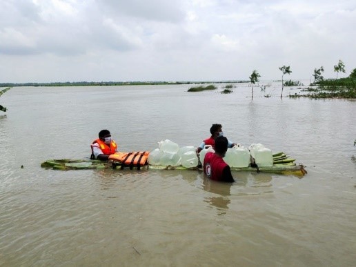 Three rescue workers wade through floodwater with a raft of clean water bottles